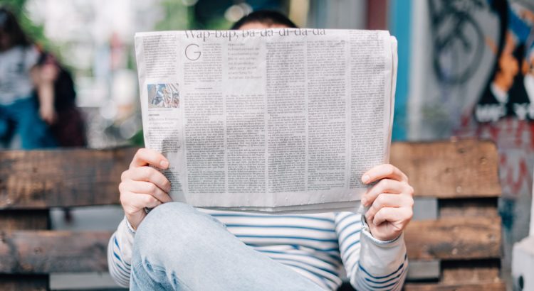 man reading newspaper on bench